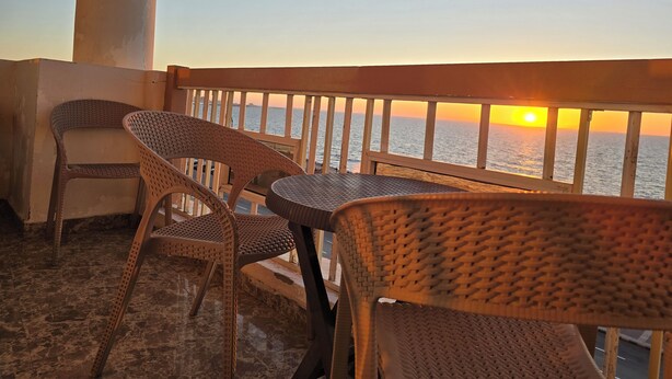 Un balcon doté de meubles en osier et offrant une vue sur le coucher de soleil sur l’eau.