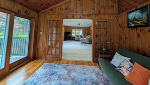 A wooden cabin interior with a cozy living area, a dining space, and a view through a large door.