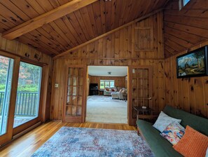 A wooden cabin interior with a cozy living area, a dining space, and a view through a large door. - Springwater Lodge, Pond & Fishing (Springwater)