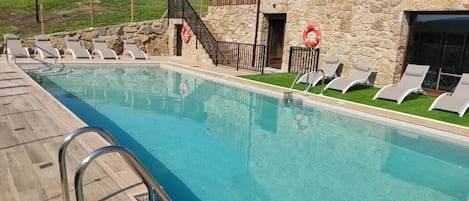 Una piscina con sillones de descanso y un edificio de piedra al fondo.