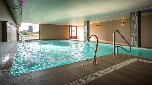 An indoor swimming pool with a view of a castle, a metal handrail, and a water fountain. - Villas Spa el Mirador de Isla (Isla)