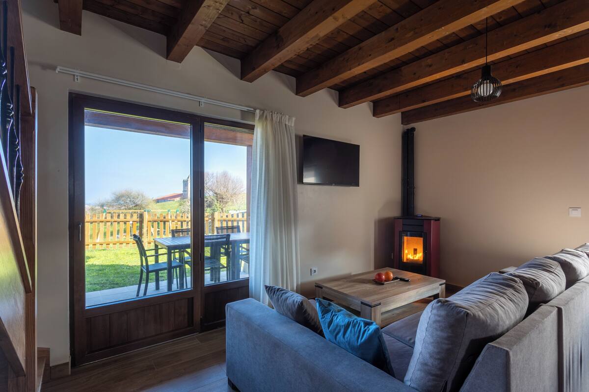 A living room with a sofa, a table with a fire, a TV on the wall, and a sliding glass door to the outside.
