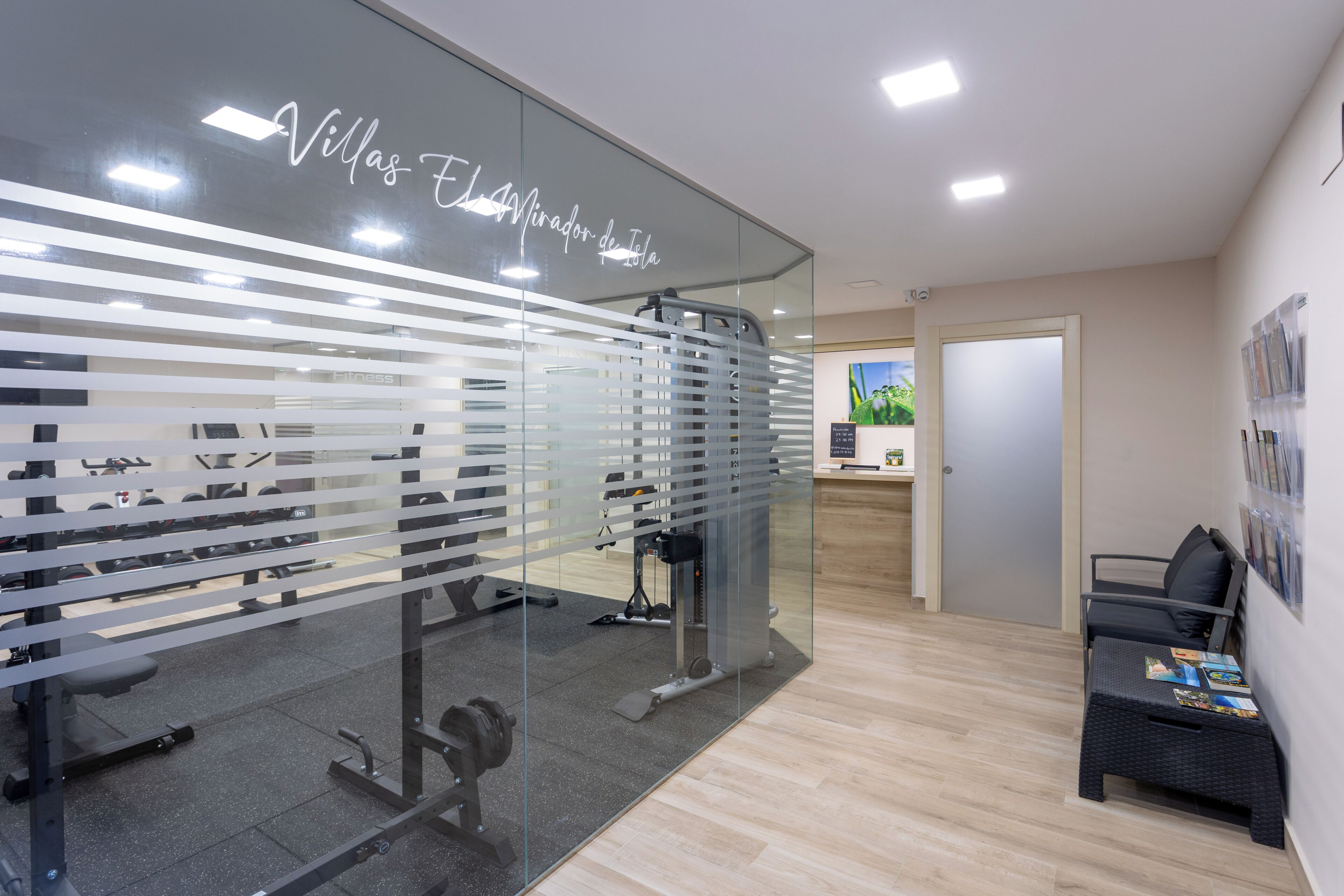 A modern interior with a glass wall, a reception desk, a seating area, and exercise equipment.