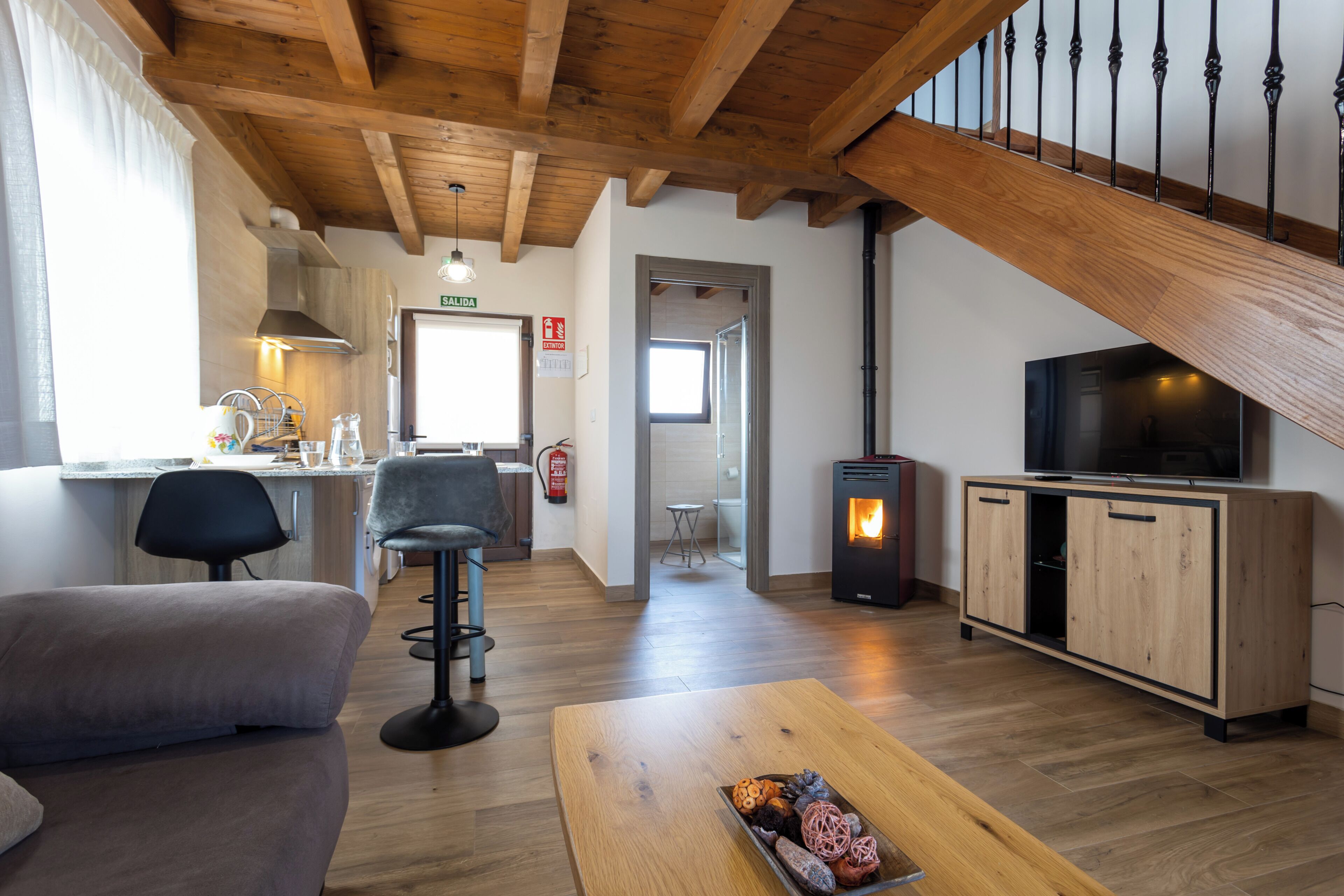 Una sala de estar moderna con un sofá, una mesa de centro con objetos decorativos, un televisor, una chimenea y una escalera.