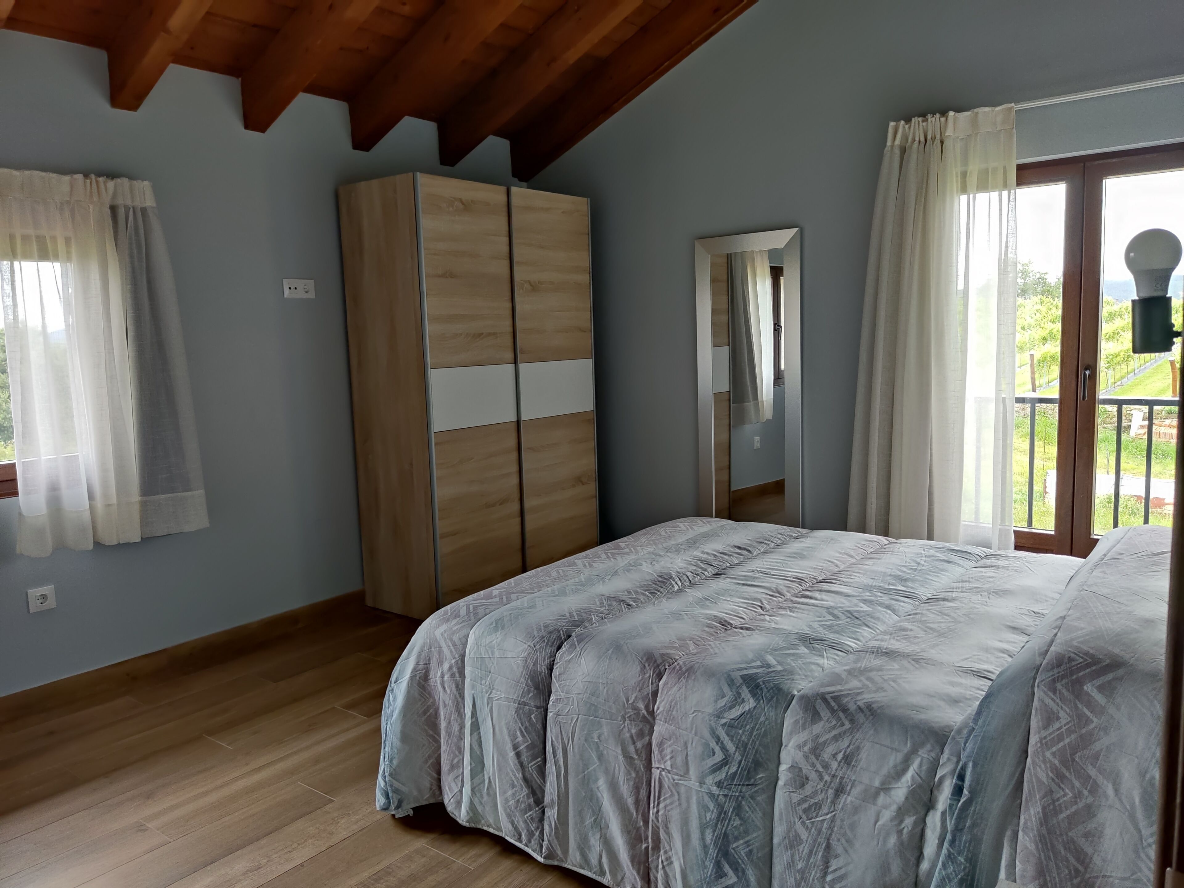 A bedroom with a bed, a wardrobe, a mirror, and a window with curtains.