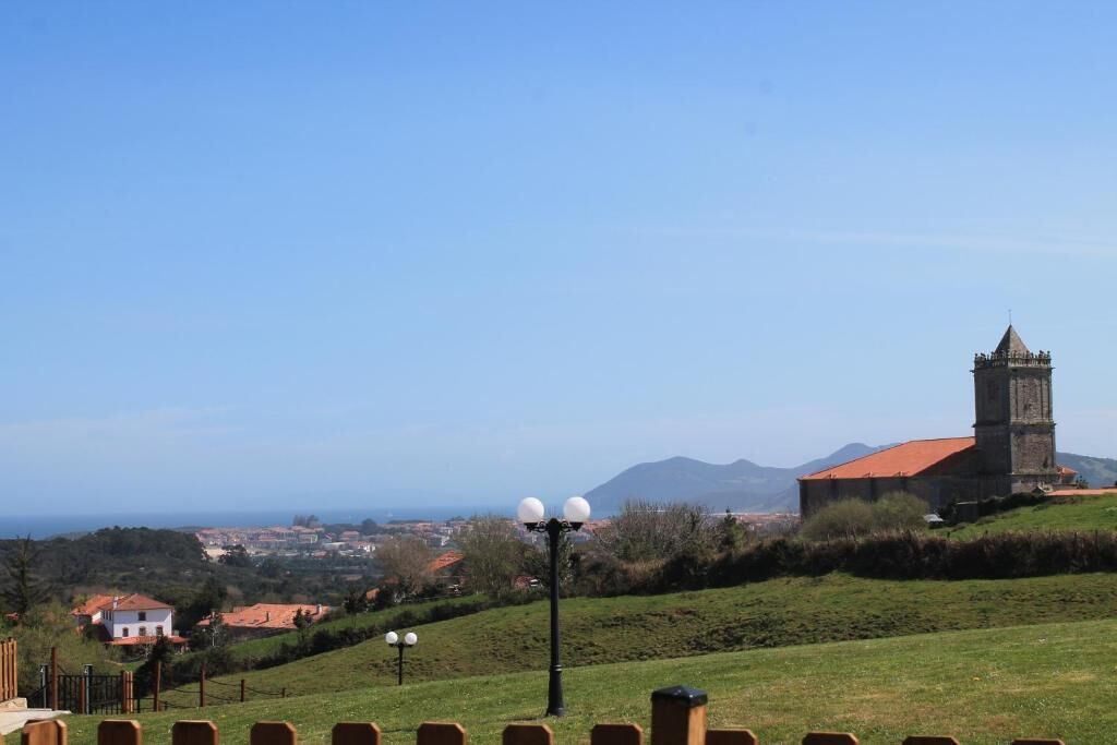 A view of a church with a bell tower, surrounded by a grassy hill and a clear sky.