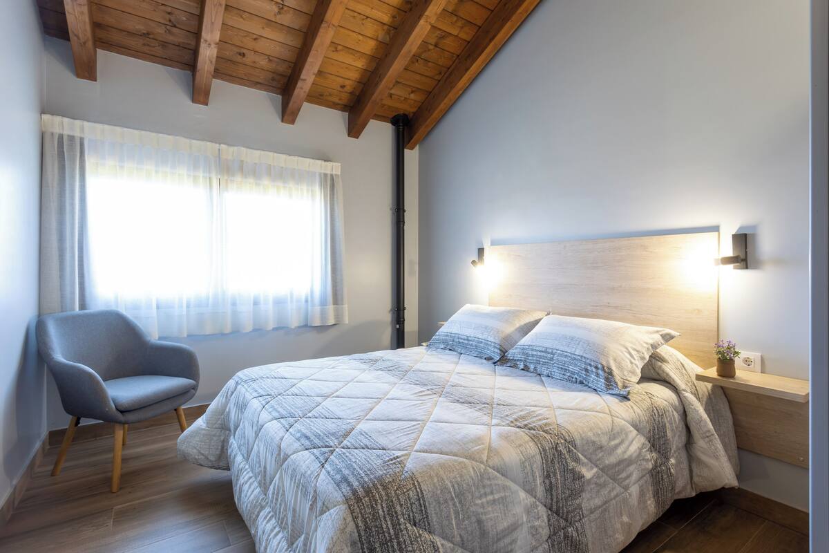 A bedroom with a bed, a chair, a nightstand, and a window with curtains.