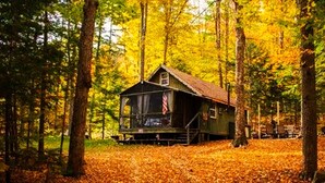 Una cabaña rodeada de un bosque con hojas otoñales.