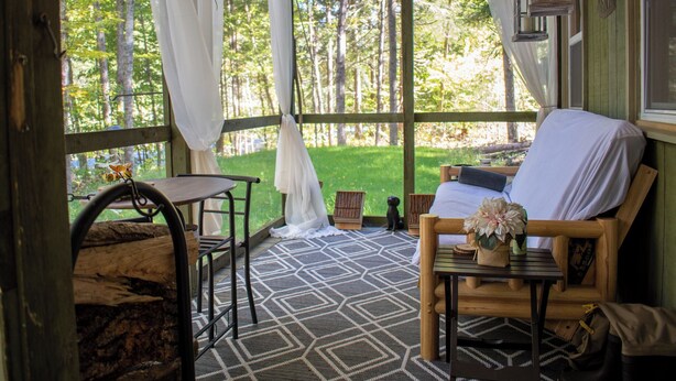 Una cabaña de madera acogedora con un porche, una cama, una mesa y una silla.