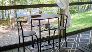 Un espacio de estar al aire libre techado, con una mesa y sillas, con vista a una zona boscosa.