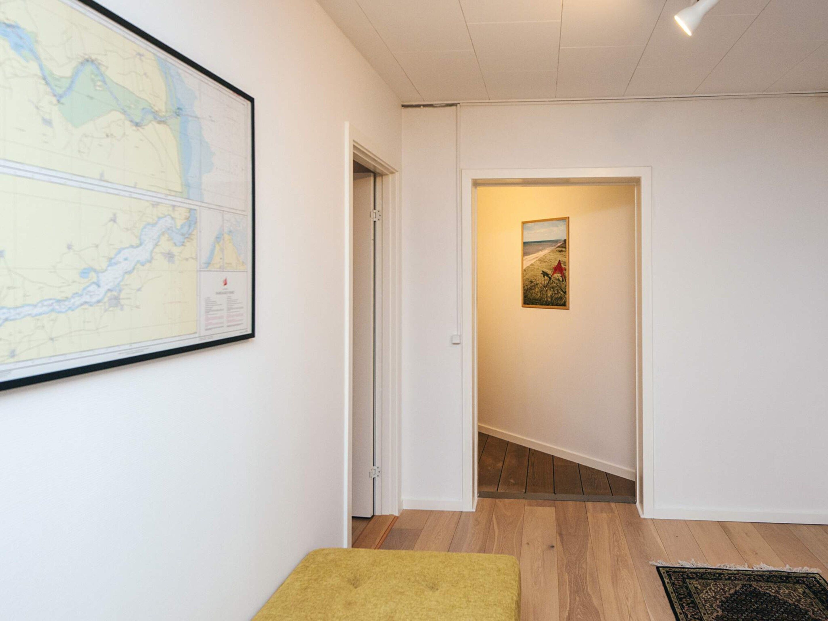 Un couloir avec une carte accrochée au mur, une porte donnant sur une autre pièce et un tapis sur le sol.