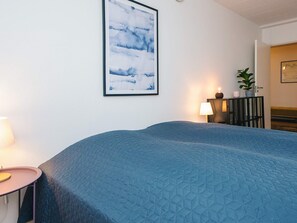 A bedroom with a large bed, a bedside table with a lamp, a framed picture on the wall, and a potted plant on a cabinet. - 10 Person Holiday Park Home in Ulfborg (Ulfborg)