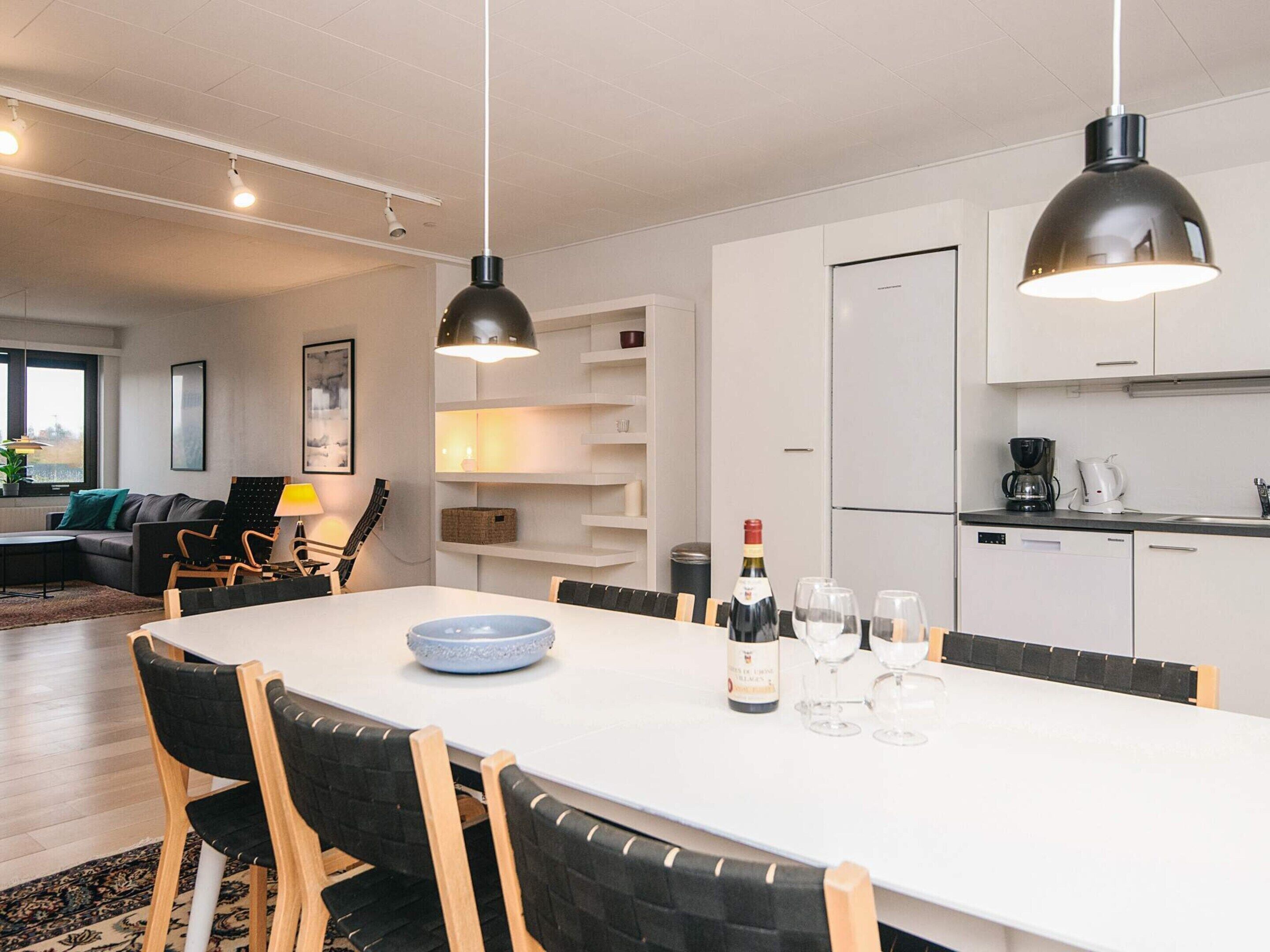 Une cuisine moderne avec des meubles blancs, une table à manger avec des chaises et un réfrigérateur.