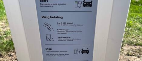 Ein Schild mit Anleitungen zur Nutzung einer Ladestation für Elektrofahrzeuge, einschließlich der Schritte zum Starten, Bezahlen und Stoppen.