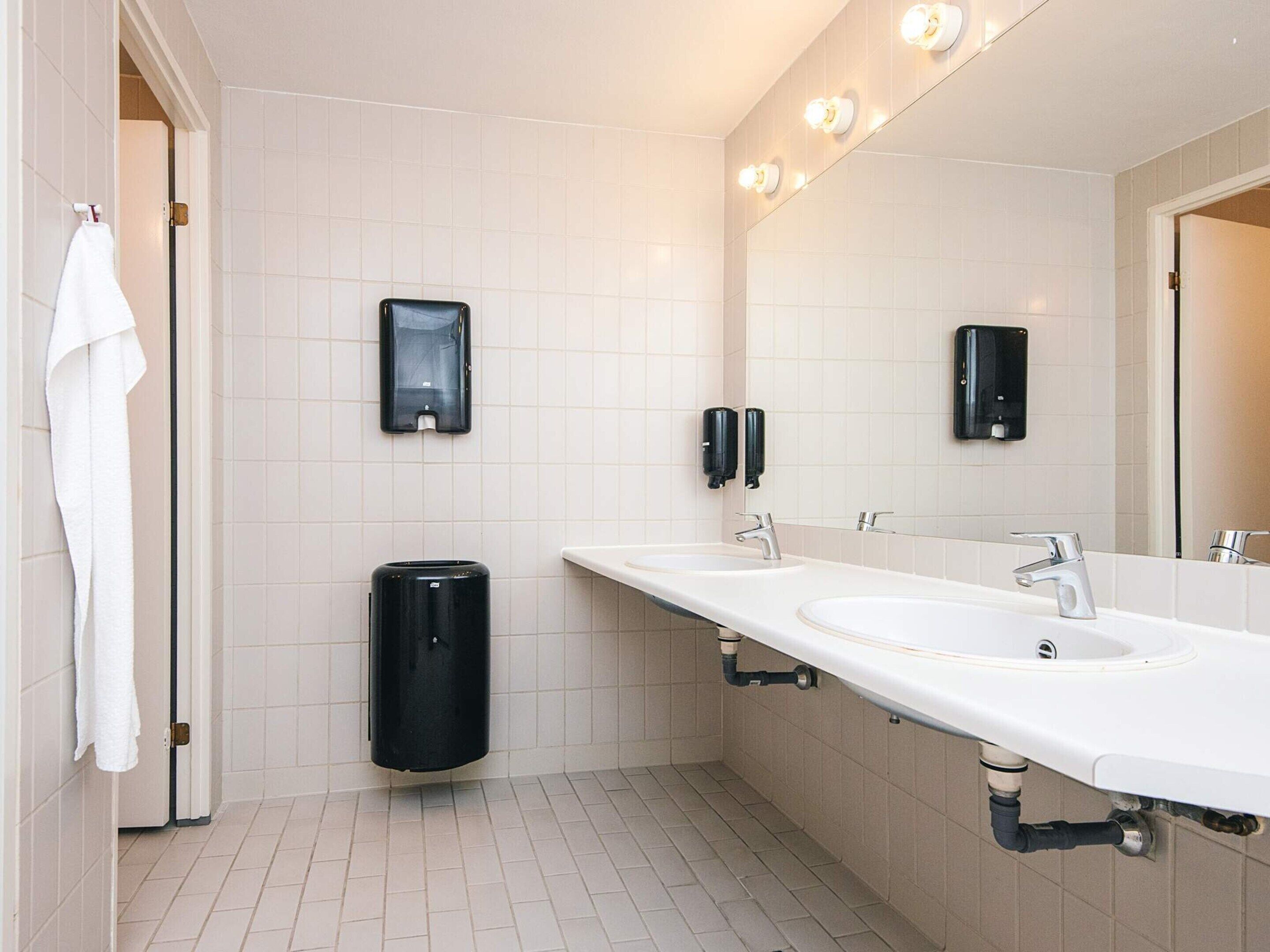 A modern bathroom with two sinks, a large mirror, and hand sanitizer dispensers.
