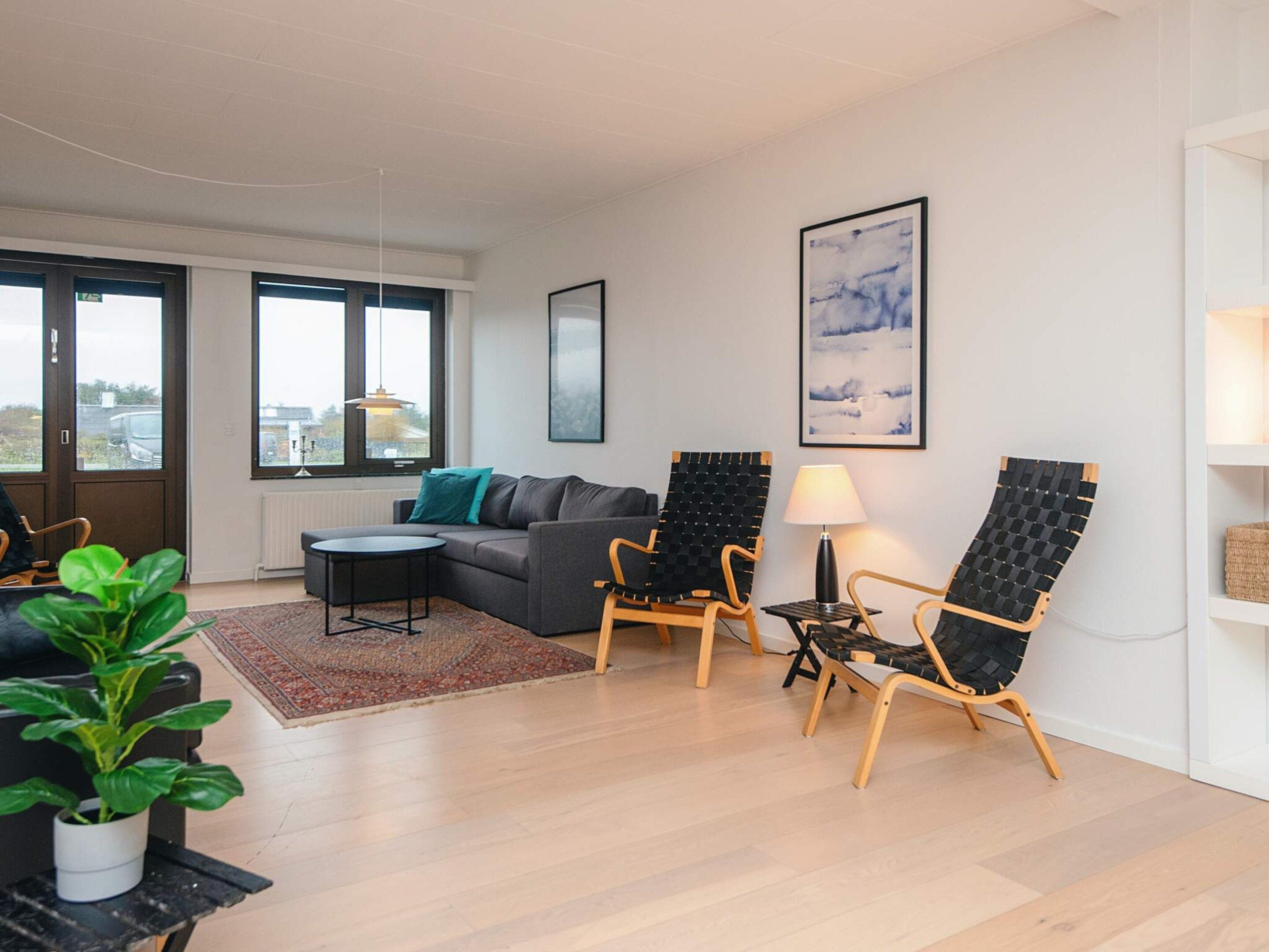 Ein modernes Wohnzimmer mit einer Couch, zwei Sesseln, einem kleinen Tisch, einer Topfpflanze und einem großen Fenster.