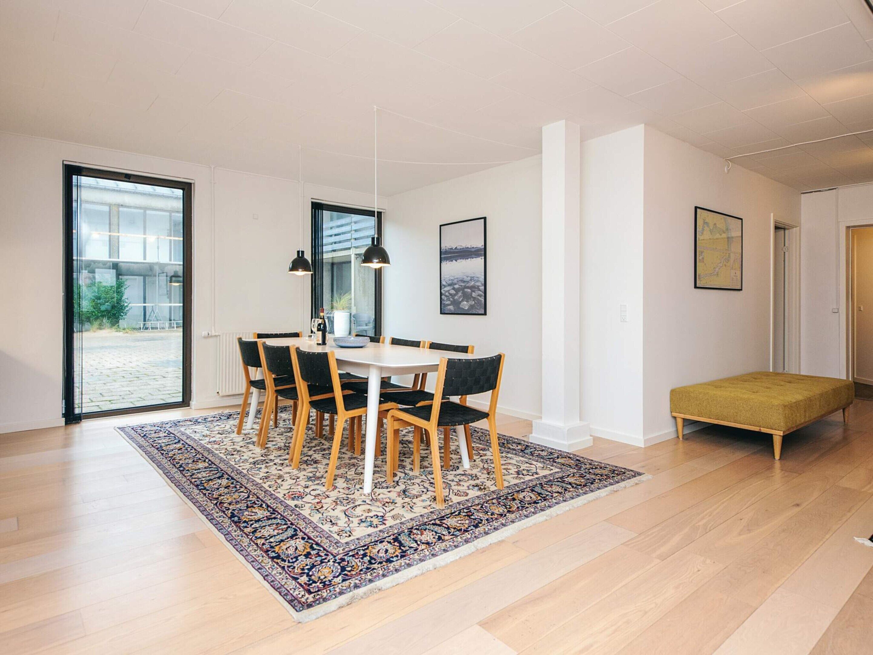 A modern dining area with a large table, chairs, and a rug.