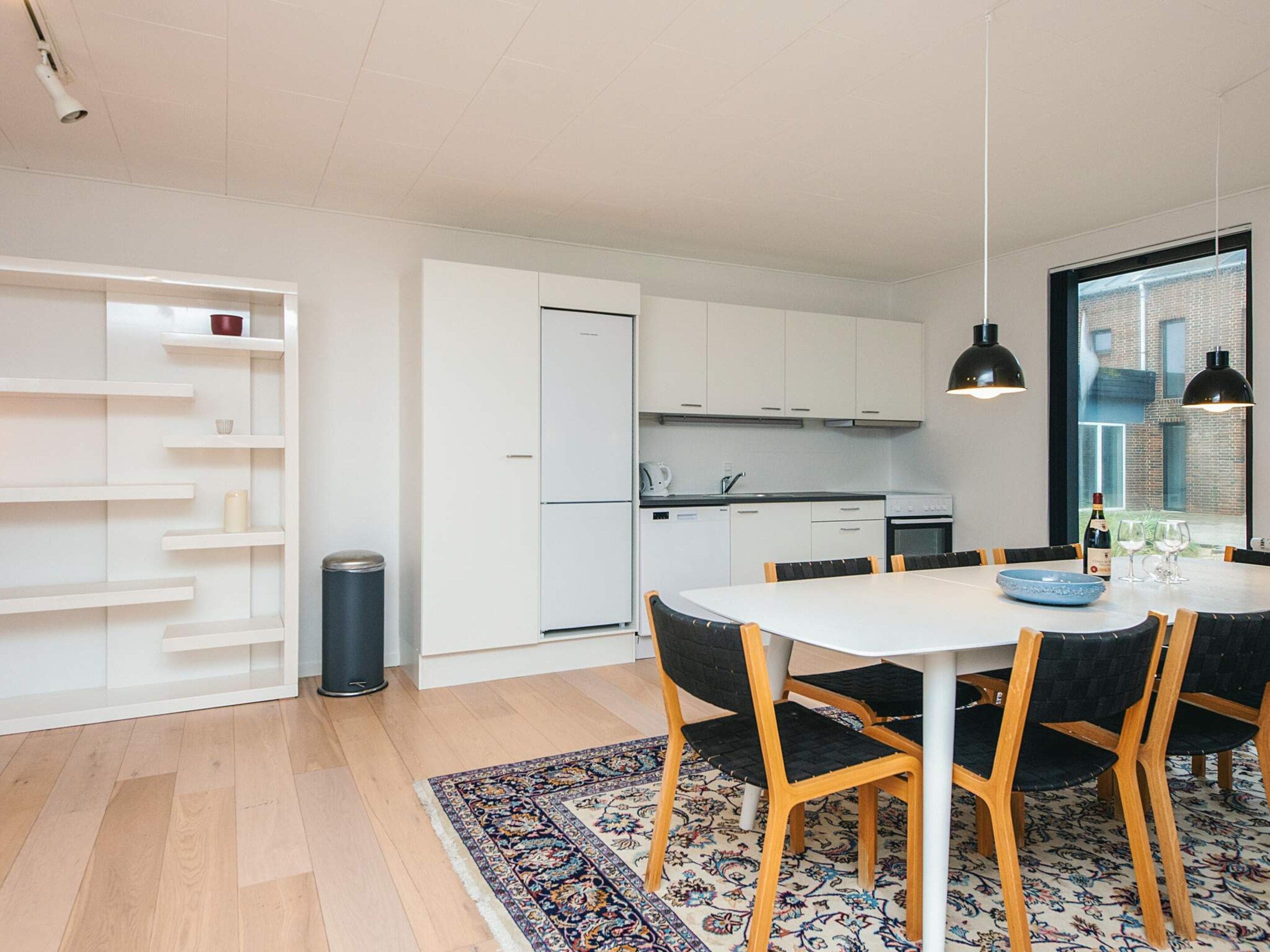A modern kitchen with white cabinets, a dining table with chairs, and a patterned rug.