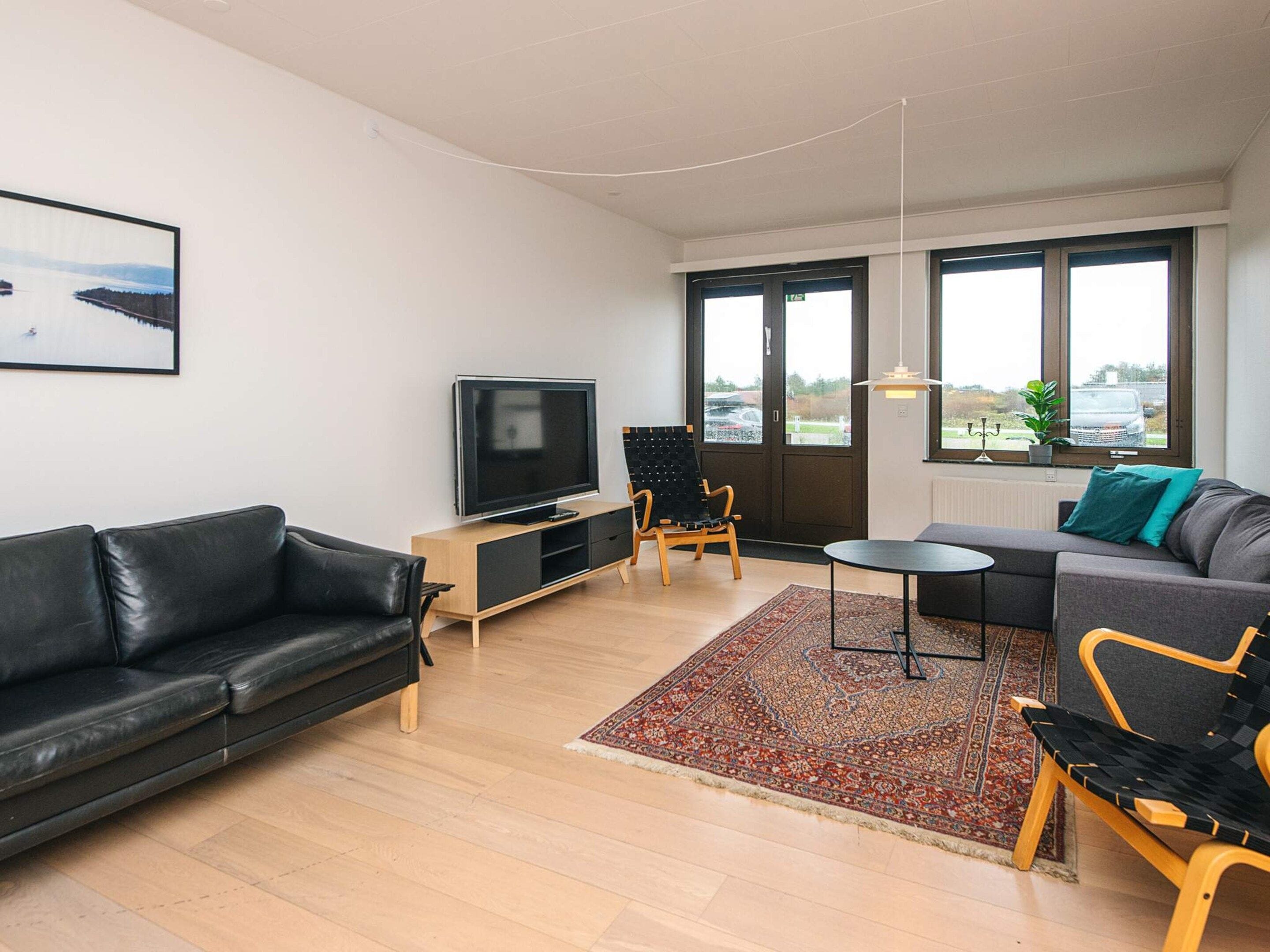 Un salon moderne avec un téléviseur à écran plat, des canapés en cuir, une table basse et un tapis à motifs.