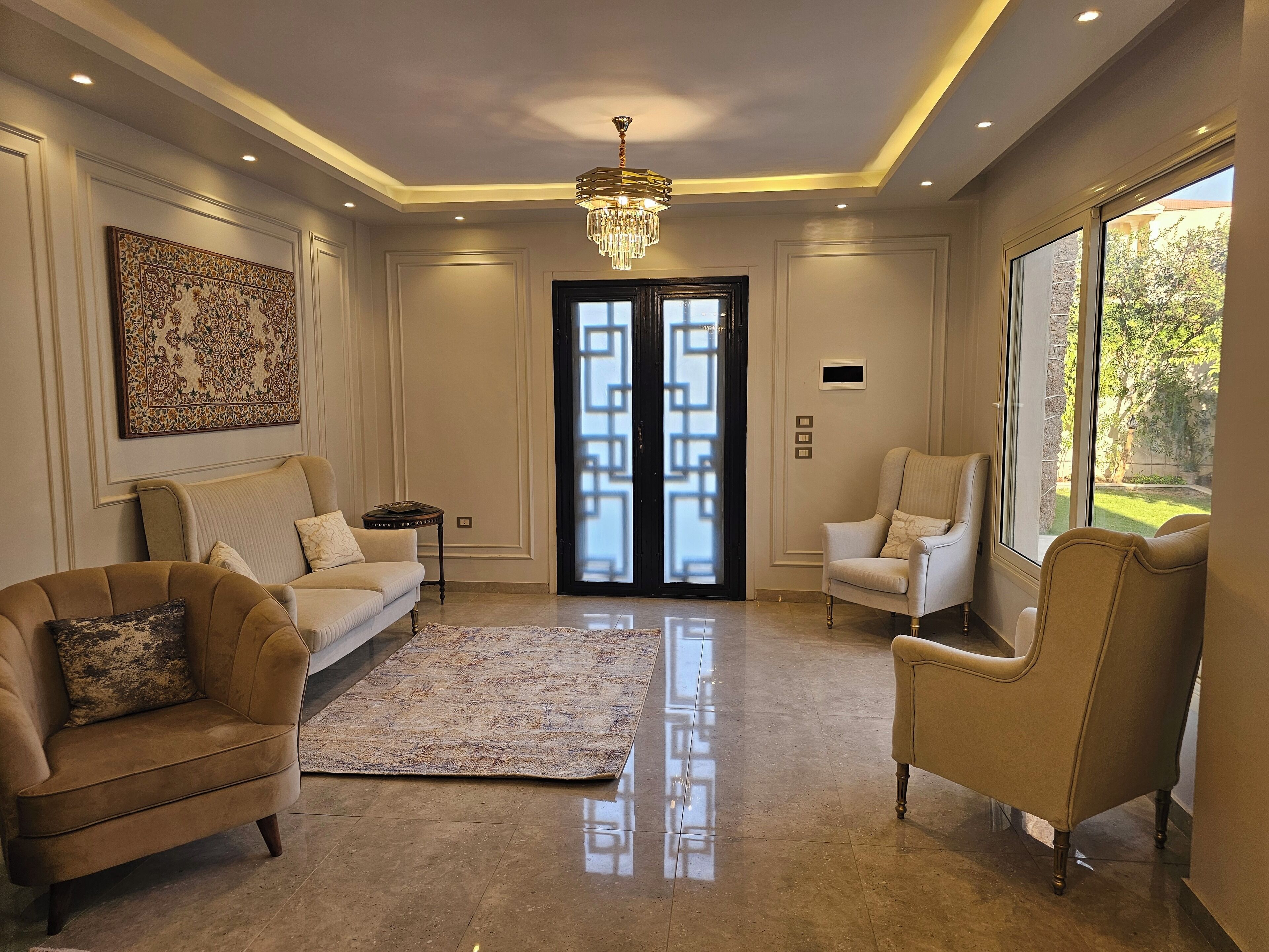 A spacious living room with a chandelier, two sofas, a rug, and a large window offering a view of the outdoors.