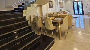 Een modern interieur met een glazen trap, een eethoek met een ronde tafel en stoelen, en een kroonluchter.
