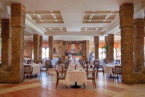A spacious dining hall with high stone columns, multiple tables, and chairs arranged for dining. - Charmillion Sea Life Resort (Qesm Sharm Ash Sheikh)
