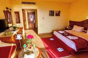 Habitación de hotel con cama, escritorio con computadora, televisor y una pequeña mesa con un jarrón y flores.