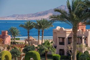 A coastal hotel with palm trees, a beach view, and mountains in the background. - Charmillion Sea Life Resort (Qesm Sharm Ash Sheikh)