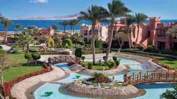 A resort with a central pool, palm trees, and a view of the sea.