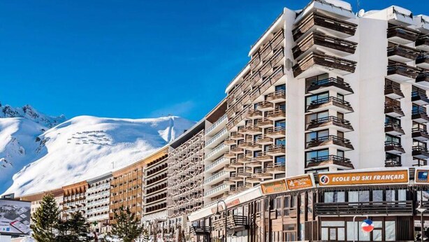 A multi-story hotel with balconies, a ski resort sign, and snow-covered mountains in the background. - Apartment in Tignes With Ski-in/ski-out (Tignes)