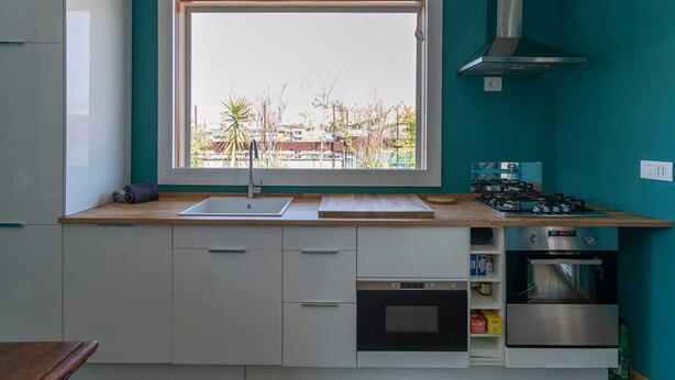 A modern kitchen with a large window, white cabinets, a built-in oven, and a gas stove. - Urban Apartment With Private Terrace (Milan)
