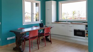 A modern kitchen with teal walls, white cabinets, a wooden dining table with red chairs, and a large window offering a view of the outdoors. - Urban Apartment With Private Terrace (Milan)