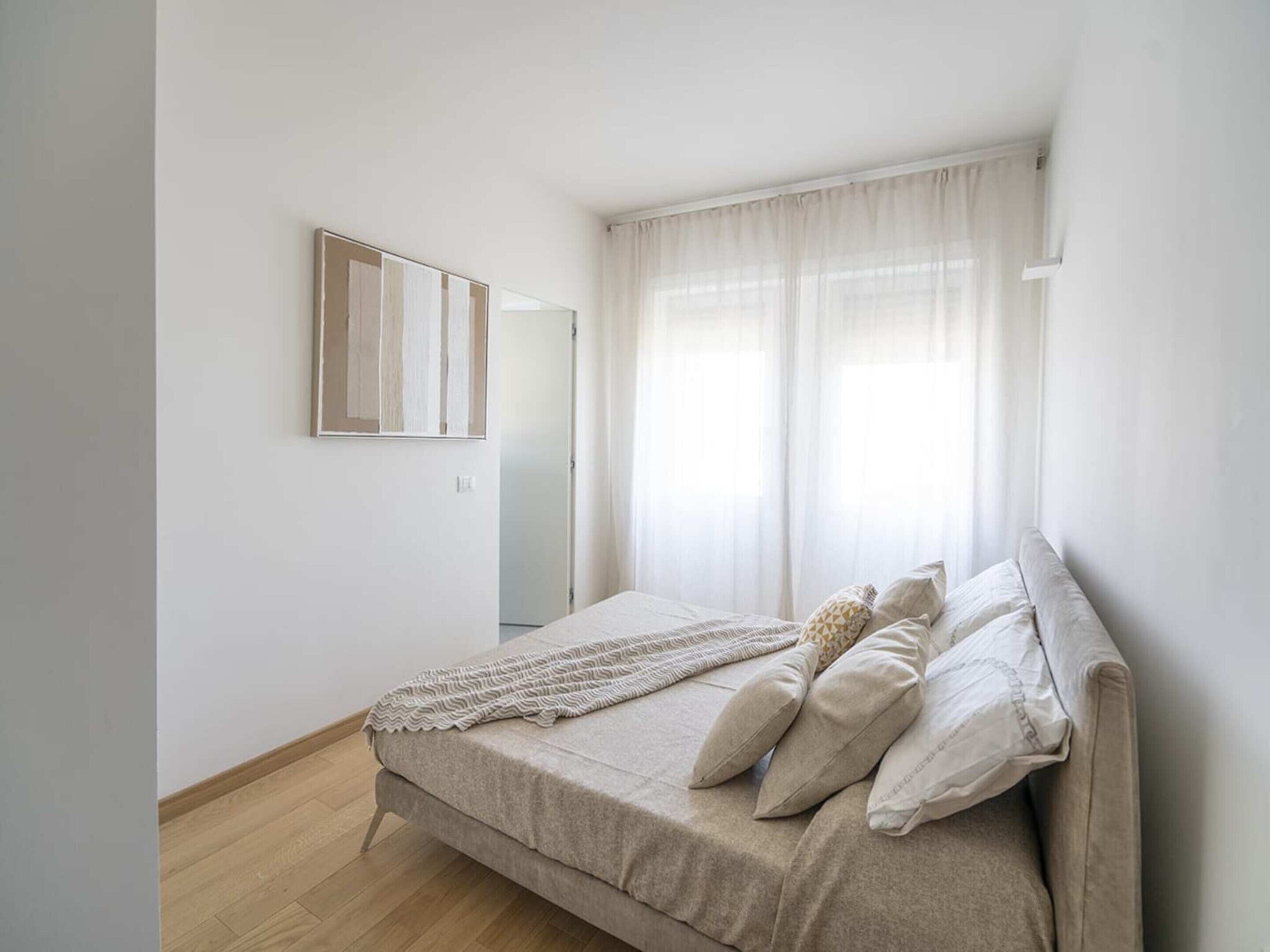 A bedroom with a bed, a mirror, and a window with curtains.
