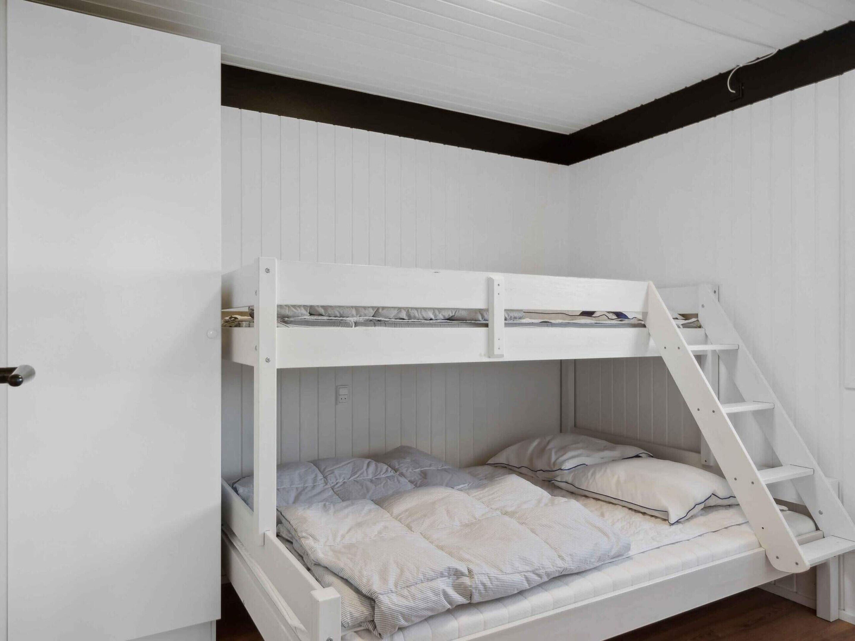 Una cama litera con escalera, paredes blancas y suelo de madera.