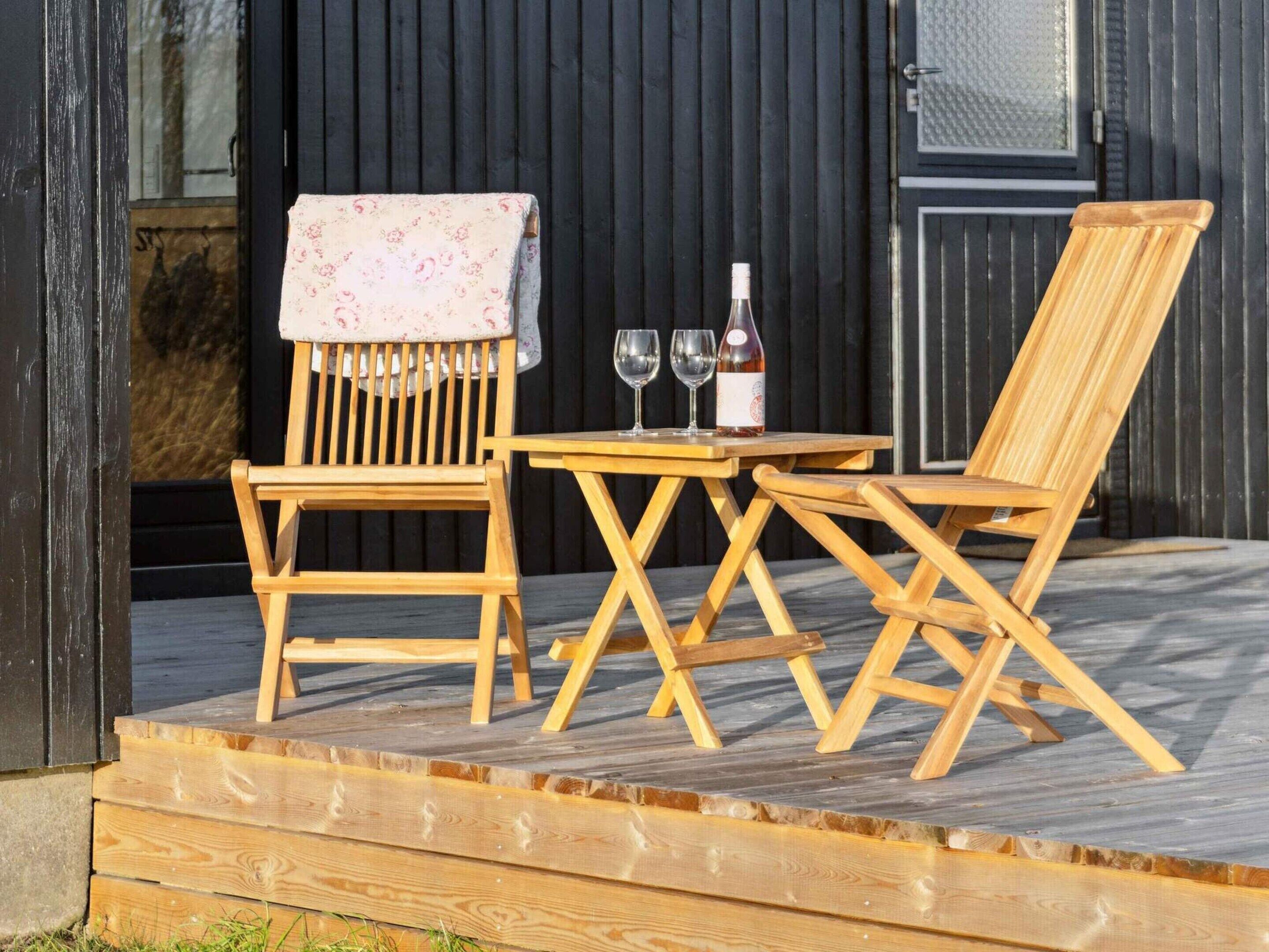 Eine Holzterrasse mit zwei Stühlen, einem Tisch, einer Weinflasche und zwei Weingläsern.