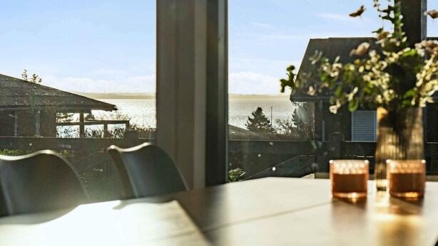 Ein Esstisch mit zwei Gläsern, einer Blumenvase und Blick auf ein Gewässer sowie Gebäude.