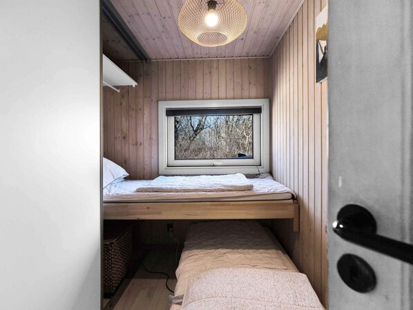 A small, cozy room with a wooden bunk bed, a window with a view of trees, and a hanging light fixture.