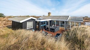 Ett modernt hus med en stor glasveranda, en terrass och utsikt över det omgivande landskapet.