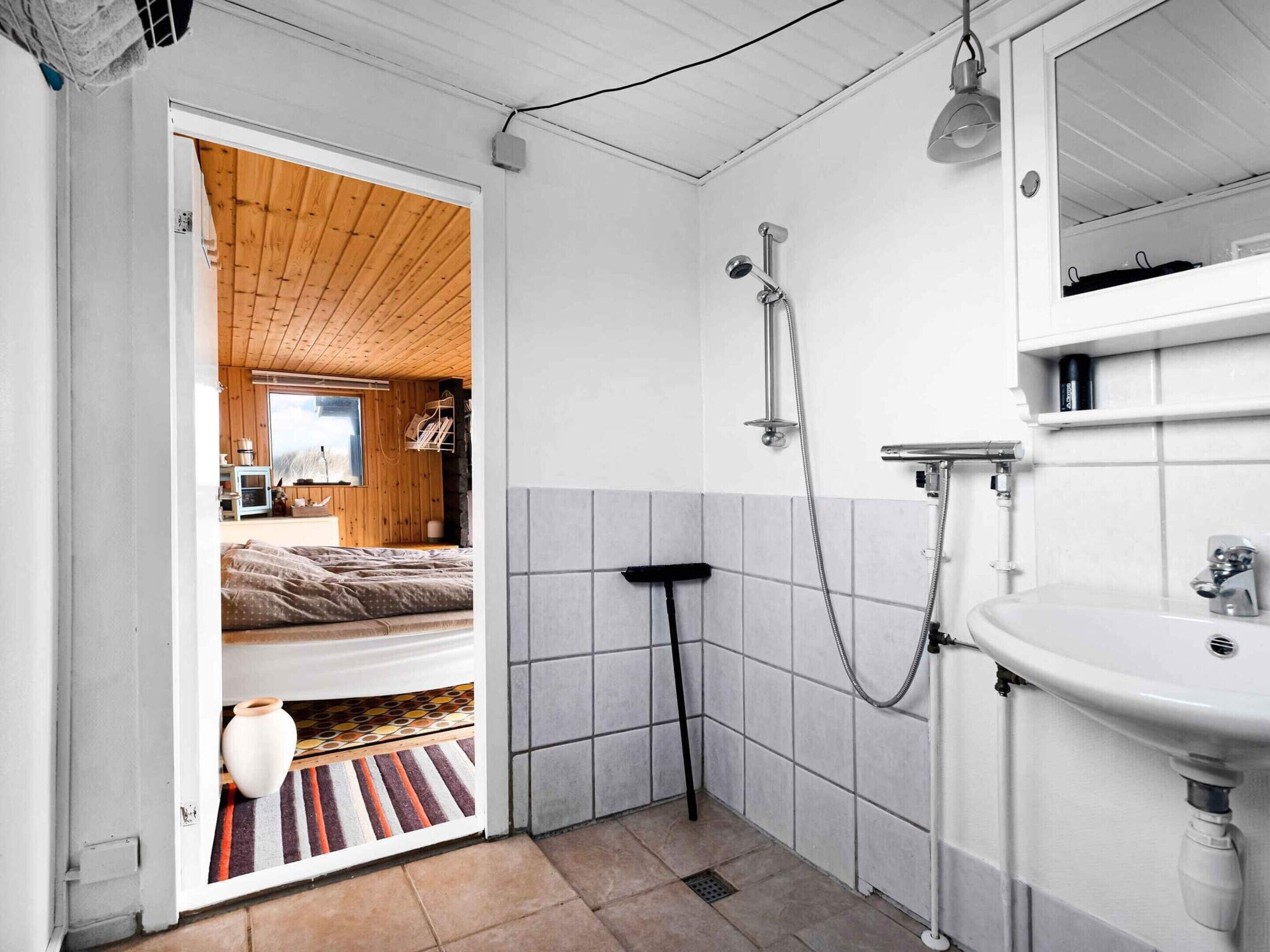 A bathroom with a shower, sink, and a wooden door leading to a bedroom.
