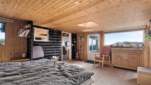 Ett sovrum i en timmerstuga med en stor säng, ett skrivbord och en stol. Det finns ett fönster med utsikt över bergen.