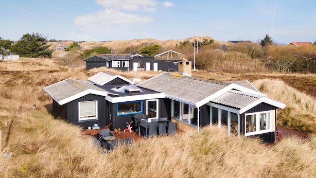 Ett modernt hus med en stor terrass, omgivet av högt gräs och sanddyner.