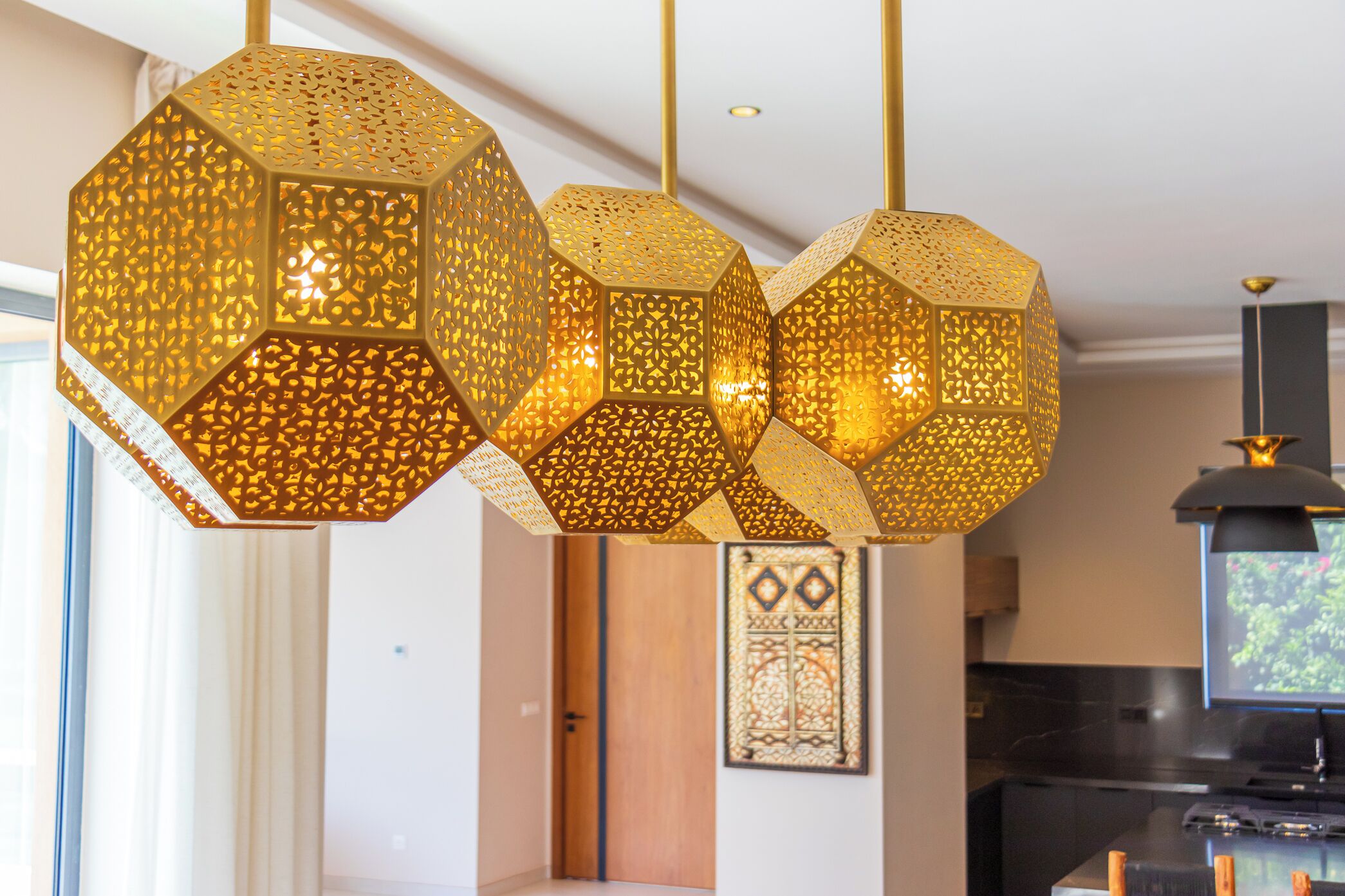 Een modern interieur met geometrische hanglampen, een houten deur en een kunstwerk in een lijst aan de muur.