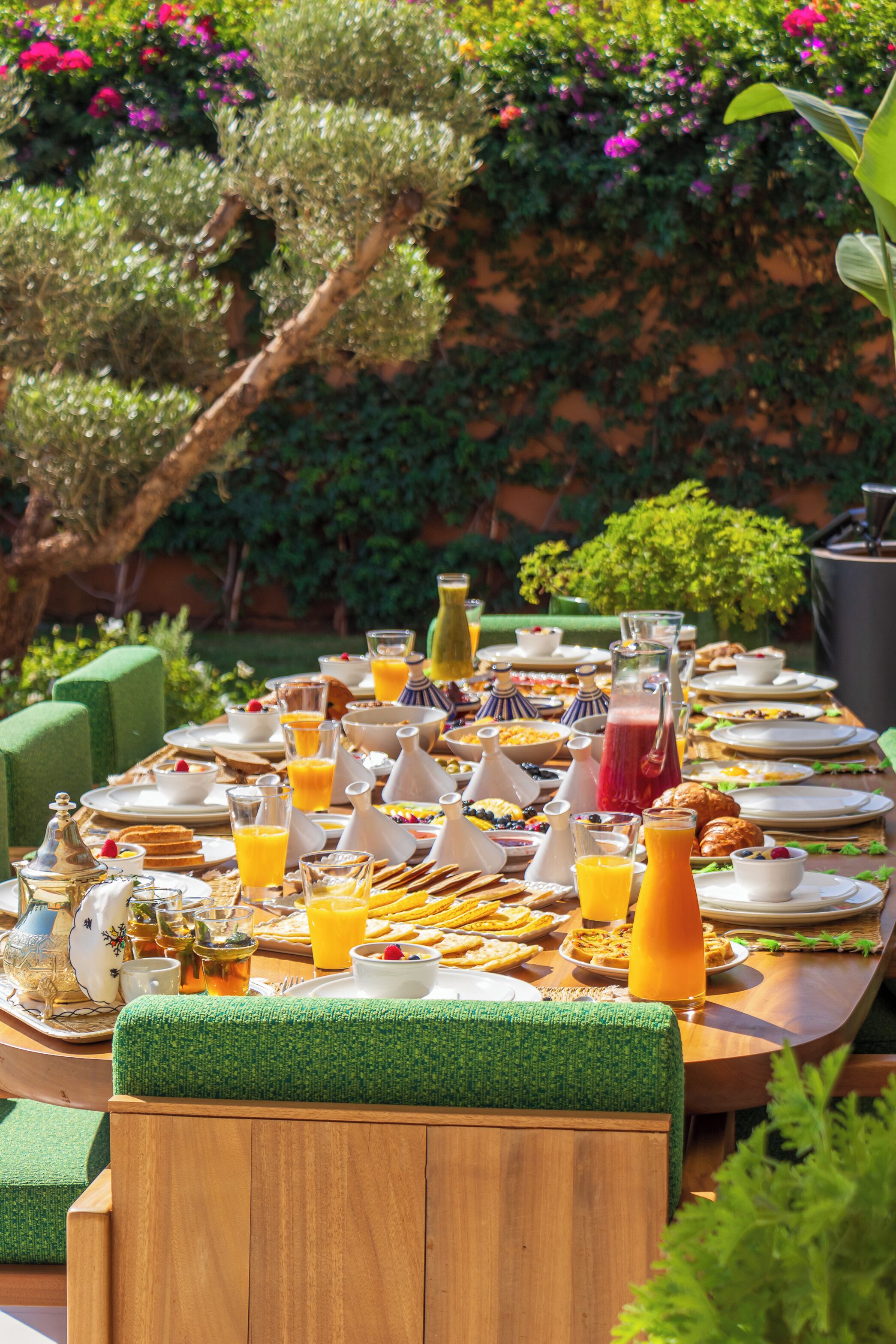 Een ontbijttafel buiten gedekt met verschillende gerechten, dranken en een kan sap.