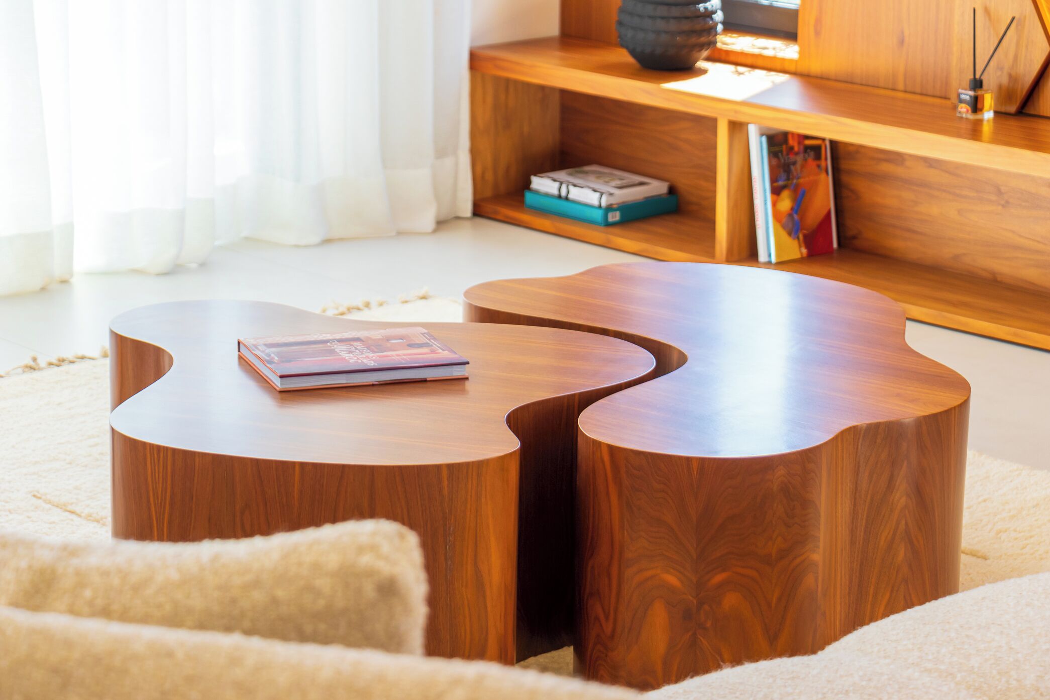 Ein modernes Wohnzimmer mit einem einzigartigen Holztisch, einer Couch und einem Bücherregal mit Büchern und Dekorationsobjekten.