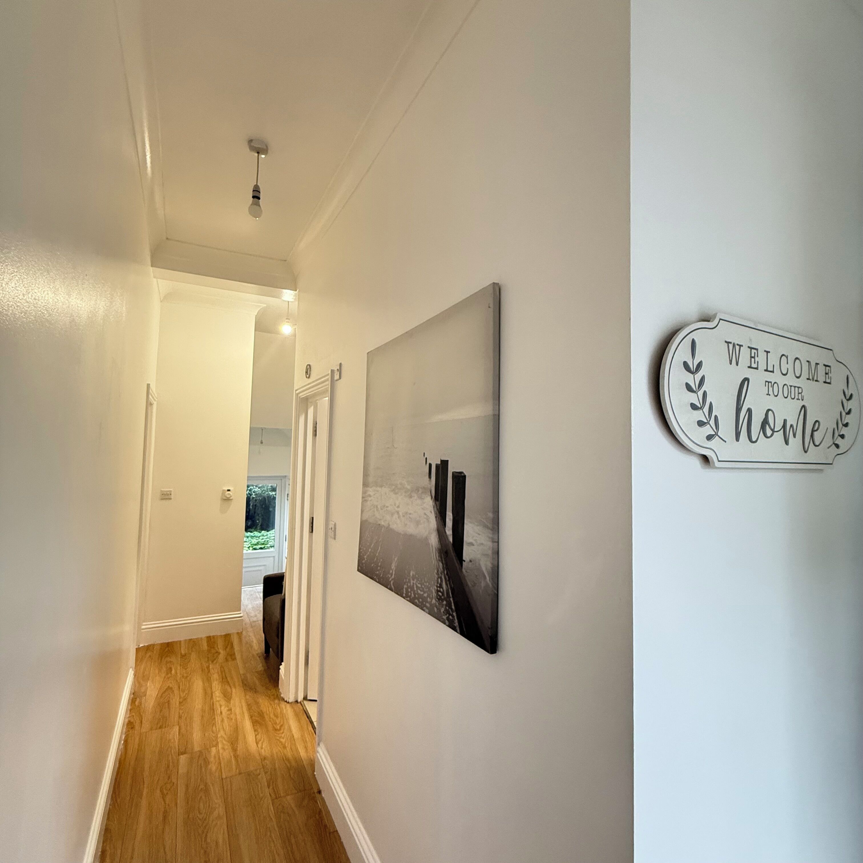 A hallway with a wooden floor, a welcome sign, and a framed picture on the wall.