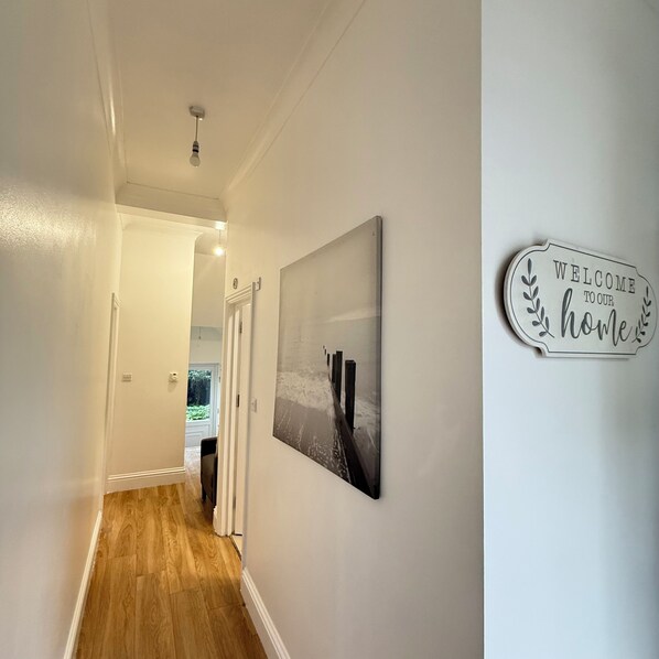 A hallway with a wooden floor, a welcome sign, and a framed picture on the wall. - The One Bed Hideaway (Croydon)
