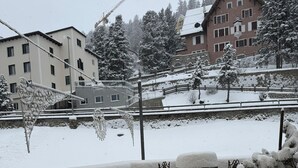 A snow-covered balcony with outdoor furniture, a view of buildings, and a snow-covered landscape. - Studio in the center, with pool and sauna, 400 mt from the ski lifts (Sankt Moritz)