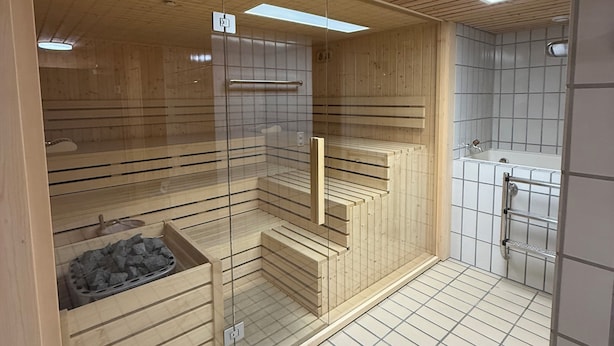 A sauna room with wooden slats, a glass door, a bench, and a tiled floor. - Studio in the center, with pool and sauna, 400 mt from the ski lifts (Sankt Moritz)
