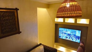 A room with a television mounted on the wall, a wicker lamp, and a framed item on the wall. - Simple sea view (families only) (Alexandria)