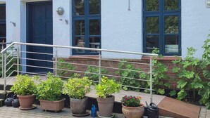 En bygning med skiltet "Gadeby Skole", hvid facade, blå døre og vinduer. Der er plantekasser med planter foran bygningen, og en metalgelænder.